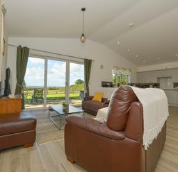An open living room and kitchen with leather sofas and a glass coffee table at The Linhay in Lapford