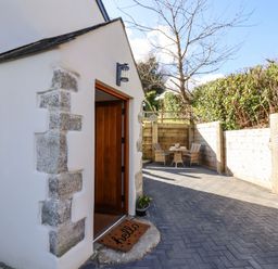 A patio area with a wooden door open and a welcome mat beside a table with chairs at The Old Chapel in Ilsington