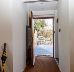An entry hallway with two umbrellas and an open wooden door showing a stone wall outside at The Old Chapel in Ilsington