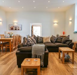 A living room with a dark sofa and wooden tables next to a dining table with six chairs at The Old Chapel in Ilsington