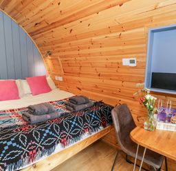 A bedroom with a double bed with folded towels and a table with flowers glasses and a bottle at Conwy Pod in Capel Garmon near Betws Y Coed