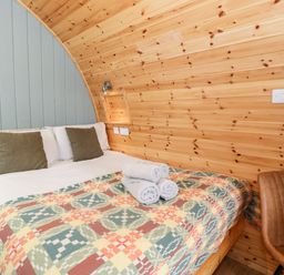 A bed with folded towels and pillows in a wooden pod room with a brown chair at Llugwy Pod in Capel Garmon near Betws-Y-Coed