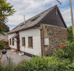Exterior of a small house with a stone and plaster wall and a garden with plants and flowers at Northwood Barn in Okehampton