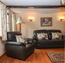 A living room with leather sofa and armchair with deer cushions a floor lamp curtains with deer pattern and a painting on the wall at Northwood Barn in Okehampton