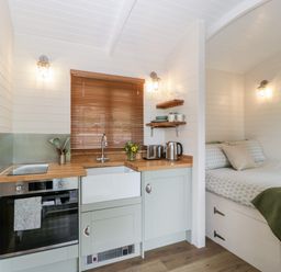 A small kitchen with an oven sink countertop toaster kettle and a bed with pillows and a blanket in a compact living space at Willow in Kemble