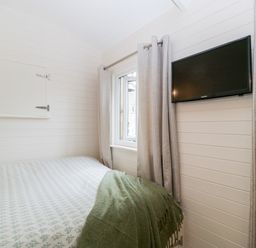 A bedroom with a bed covered in patterned bedding a green blanket a window with curtains and a wall-mounted television at Willow in Kemble