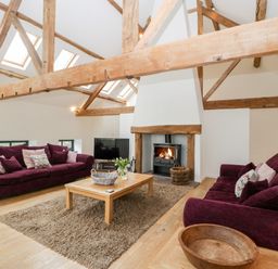 A living room with exposed wooden beams a fireplace two purple sofas a wooden coffee table and a television at Owl Barn in Marston Stannett near Leominster