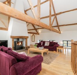 A living room with purple sofas a fireplace wooden beams and a coffee table at Owl Barn Marston Stannett near Leominster