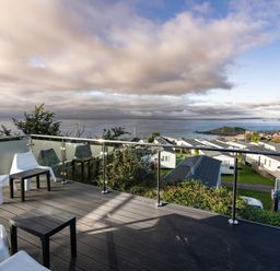 A balcony with white chairs and black tables overlooking cabins and the sea at Lanyon in St Ives