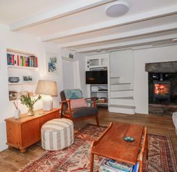 A living room with a lamp, television, and fireplace at Ivy Cottage in Trenale near Tintagel