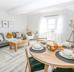 A living room and dining area with a gray sofa orange cushions wooden table and round dining table set with dishes at Sea La Vie in Benllech
