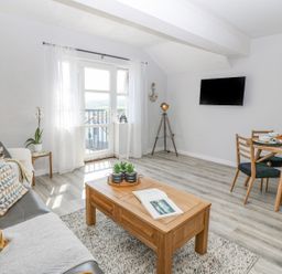 A living room with a sofa and coffee table and a dining table with chairs and a wall-mounted TV at Sea La Vie in Benllech