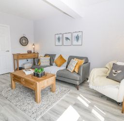 A living room with a gray sofa and white armchair wooden coffee table and console table with wall clock and framed pictures at Sea La Vie in Benllech