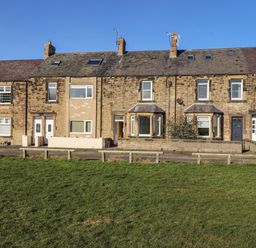 A row of stone terraced houses with front doors and windows facing a green lawn at Southview Amble in Amble