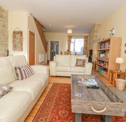 A living room with two cream sofas a wooden coffee table a red patterned rug a wooden bookshelf and a stone fireplace at Southview Amble in Amble