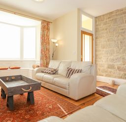 A living room with white sofas a stone wall a wooden coffee table and a bay window with cushions at Southview Amble in Amble