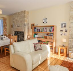 A living room with a white sofa, bookshelf, dining table with chairs, and stone fireplace at Southview Amble in Amble