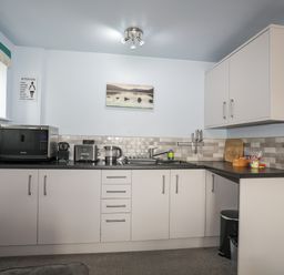 A kitchen with white cabinets a microwave toaster kettle knives and a sink at Tegid Lakeside - Bala Lake in Bala