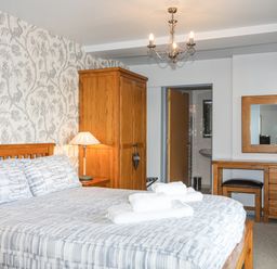 A bedroom with a double bed with towels on it a wooden wardrobe a bedside table with a lamp a dressing table with a mirror and stool at Tegid Lakeside - Bala Lake Bala