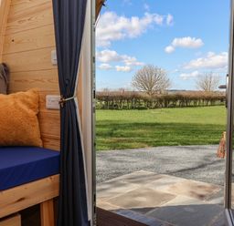 An open door leading to a garden with grass trees and hedges viewed from a room with a wooden bench blue cushion and yellow pillow at Covey in Little Kelk near Bridlington