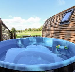 An outdoor hot tub with rubber ducks next to a wooden building and a grassy field in the background at Covey in Little Kelk near Bridlington