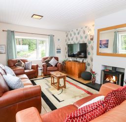 A living room with leather sofas a wooden coffee table a wall-mounted television and a fireplace at Willoway in Benllech
