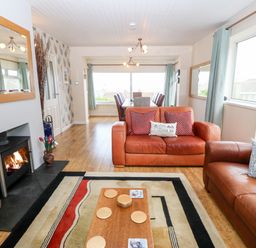 A living room with two brown leather sofas a fireplace wooden floor and a dining area at Willoway in Benllech