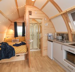 A compact wooden cabin interior with a bed a shower kitchen appliances and a small fridge at Bevy Little Kelk near Bridlington