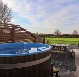 An outdoor area with a hot tub wooden picnic table and a grass field with a soccer goal at Bevy in Little Kelk near Bridlington