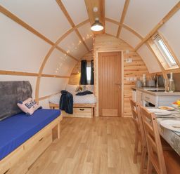 An arched room with a wooden floor a blue sofa a bed a dining table set with plates and a kitchen area Husk Little Kelk near Bridlington