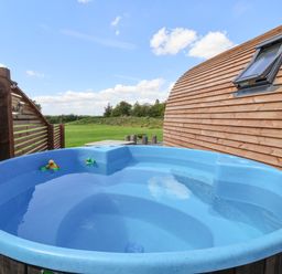 An outdoor hot tub with rubber ducks next to a wooden building and a fenced lawn at Husk in Little Kelk near Bridlington