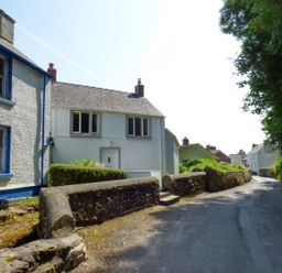 A narrow road lined with stone walls and white houses with blue trim at Spring Garden Cottage in Laugharne