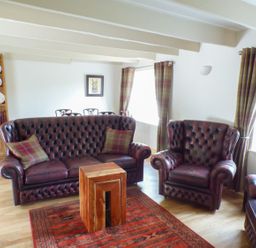 A sitting room with leather sofas wooden table patterned rug and plate rack at Spring Garden Cottage in Laugharne