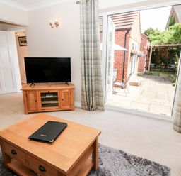 A living room with a wooden coffee table a television on a wooden stand and an open door leading to a patio at Church View in Withernwick near Aldbrough