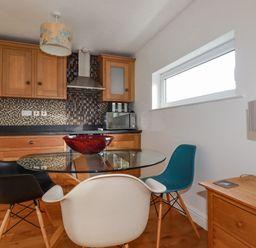 A kitchen with wooden cabinets and a black countertop with a glass table and three chairs at Lapwing in Perranporth