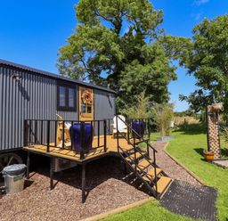 A small grey cabin with a wooden deck and two chairs in a garden with trees at Portland Luxury Glamping in Nottingham