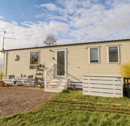 A single-story mobile home with a small patio table and chairs and potted plants outside at 46 Willowburn in Felton
