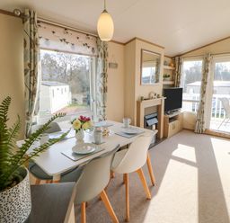 A dining area with a table set for four next to large windows and a living space with a TV and fireplace at 46 Willowburn in Felton
