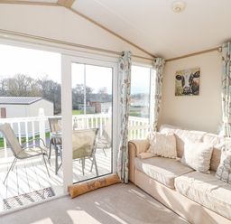 A living room with beige sofa and cushions next to glass sliding door opening to patio with table and chairs at 46 Willowburn in Felton