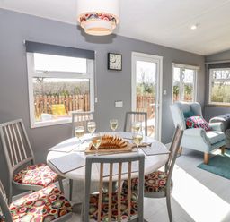 A dining area with a round table set with glasses and bread and chairs with patterned cushions next to a living room with armchairs and a sofa at Cwrt y Ceffyl in Boduan near Morfa Nefyn