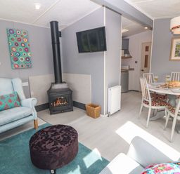 A living room with armchairs a fireplace a wall-mounted television and a dining area with a table and chairs at Cwrt y Ceffyl in Boduan near Morfa Nefyn