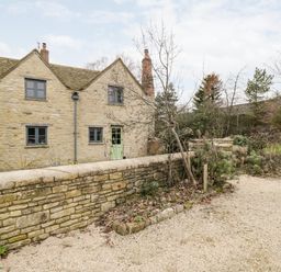 An exterior view of a stone house with a gravel driveway and a low stone wall at High Cogges Farm Holiday Cottages Witney