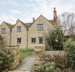 Stone cottage with multiple windows and a green door behind a stone wall garden at High Cogges Farm Holiday Cottages in Witney