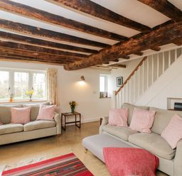 A living room with two sofas with pink cushions a staircase and wooden ceiling beams at High Cogges Farm Holiday Cottages in Witney
