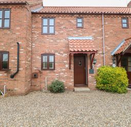 A brick house exterior with two brown doors and four windows with gravel in front at 10 Ruston Reaches East Ruston near Stalham
