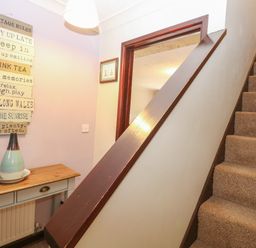 A staircase next to a wooden table with a vase and decorative sign on the wall at 10 Ruston Reaches East Ruston near Stalham