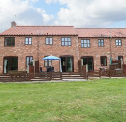 A rear view of terraced brick houses with fenced patios and outdoor furniture on a lawn at 10 Ruston Reaches in East Ruston near Stalham