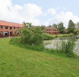 A row of brick houses with brown roofs beside a pond and a grassy area at 10 Ruston Reaches in East Ruston near Stalham