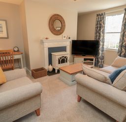 A living room with two beige sofas around a wooden coffee table near a fireplace a TV on a stand and patterned curtains at Charter's Cottage in Berwick-Upon-Tweed
