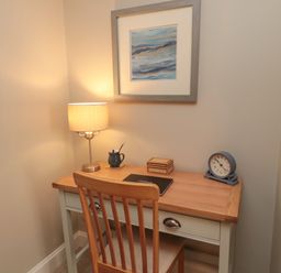 A wooden desk with a chair a lamp a clock a small box a mug and a picture on the wall at Charter's Cottage in Berwick-Upon-Tweed